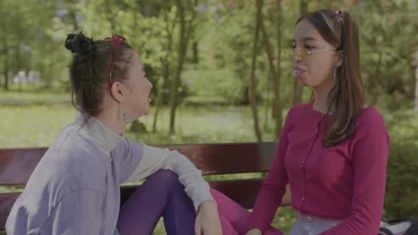 Girl blowing bubbles of chewing gum. Girls play with chewing gum on a park bench. — Stock video