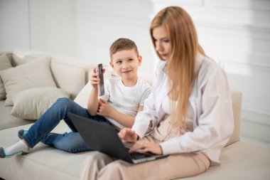 Bilgisayarda çalışan meşgul bir anne. Oğlu annesine komik videolar gösteriyor. Annem evde bebekle birlikte çalışıyor..