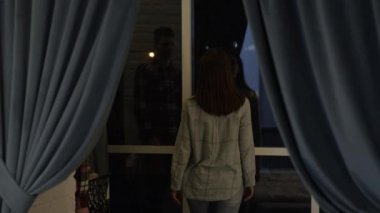 Genç adam nazikçe pencerenin kenarında duran ve şehir manzarasına hayran olan sevgilisine sarılıyor..