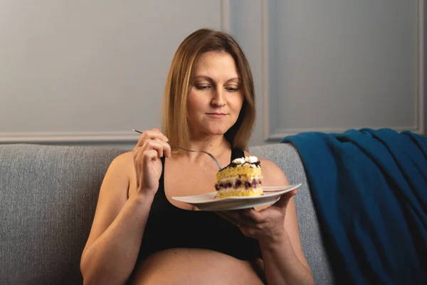 Hamile bir kadın bir dilim pastayla bir tabak tutar ve onu yemeye hazırlanır. Yatay fotoğraf.