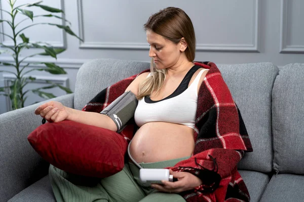 Беременная Женщина Измеряет Артериальное Давление Сидя Диване Одета Домашнюю Одежду Стоковое Фото
