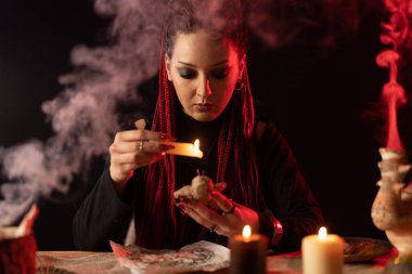 The witch performs a ritual with a voodoo doll. Witchs room. Against the background of smoke from candles.