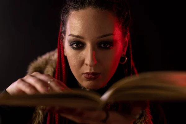 Witch face close up. Mystical woman on a black level holds a hand on a book. A piercing look and dark make-up.