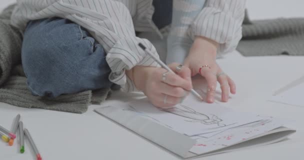 这个女孩画了一个衣服模型 你的手指上有很多不同的戒指那姑娘坐在地上画画 — 图库视频影像