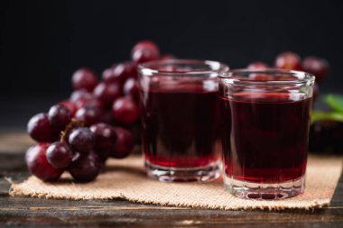 Bardakta kırmızı üzüm suyu, ahşap arka planda taze üzüm, sağlıklı içecek, natürmort.