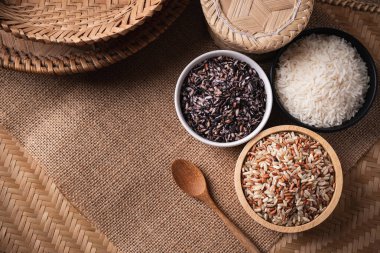 Kahverengi zemin üzerinde bir kasede çeşitli organik Tayland pirinç taneleri (kahverengi, beyaz ve mor pirinç), masa üstü görünümü