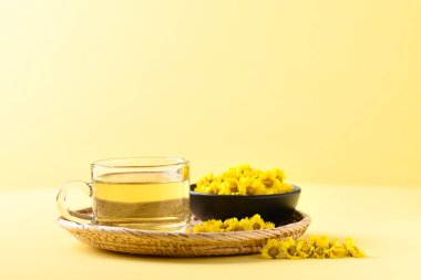 Sarı arka planda bir fincanda organik kasımpatı çiçeği çayı, sağlıklı bitkisel içecek.