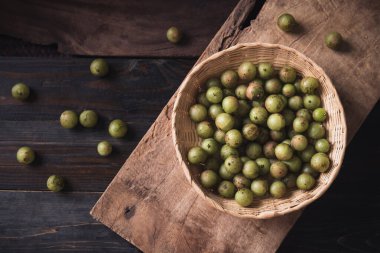 Tahta arka planda bambu sepetinde yabani Hint bektaşi üzümü veya amla, Asya 'da meyve ağacı çeşitli mutfaklarda, bitkisel ilaçlarda ve zengin C vitamininde kullanılır.