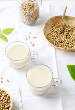 Bardakta soya sütü, bambu sepetinde soya fasulyesi ve beyaz arka planda kase, sağlıklı içecek.
