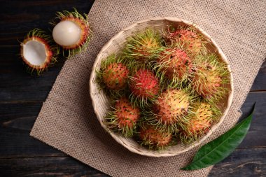 Tahta arka planda bambu sepetinde olgun Rambutan meyvesi, tropik meyve ve yerli Güneydoğu Asya, sulu ve tatlı bir tat.