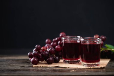 Bardakta kırmızı üzüm suyu, ahşap arka planda taze üzüm, sağlıklı içecek, natürmort.
