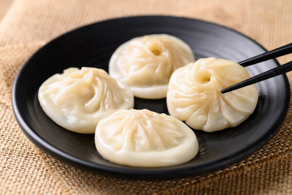 Сяо лонг бао, маленькая китайская тушеная булочка с фаршем из свинины на черной тарелке, которую едят с помощью палочек