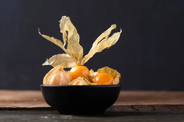 Cape gooseberry or golden berry (Physalis peruviana) in black bowl on wooden background, Healthy tropical fruit