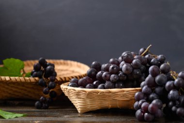 Bambu sepetinde kırmızı üzüm, tahtanın üzerinde siyah arka planda.