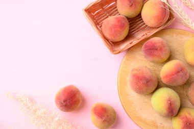 Şeftali meyvesi tahtada ve sepet pembe arka planda.