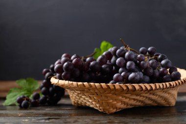 Bambu sepetinde kırmızı üzüm, tahtanın üzerinde siyah arka planda.