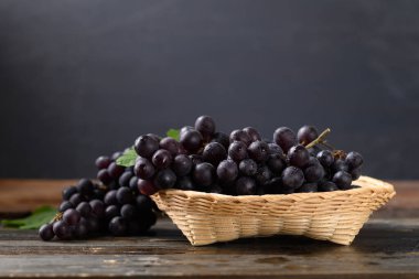 Bambu sepetinde kırmızı üzüm, tahtanın üzerinde siyah arka planda.