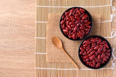 Tahta arka planda kaşıkla kasede kırmızı böbrek fasulyesi, masa üstü görünümü.