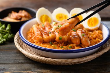 Tteokbokki 'li Kore baharatlı hazır şehriye, ahşap arka planda sosis ve yumurta.