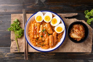Tteokbokki 'li Kore baharatlı hazır şehriye, ahşap arka planda sosis ve yumurta, masa üstü manzaralı.