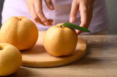 Ahşap arka planda kadın eli olan Asya armudu ya da Nashi armudu.