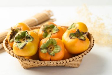 Ripe persimmon fruit in basket on white background