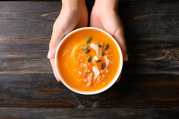 stock image Butternut squash pumpkin soup in bowl holding by hand on wooden background, Homemade food in autumn season