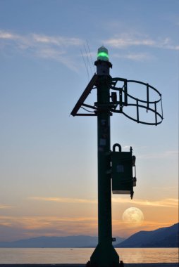 beautiful sunset at the sea with full moon behind the boats marker