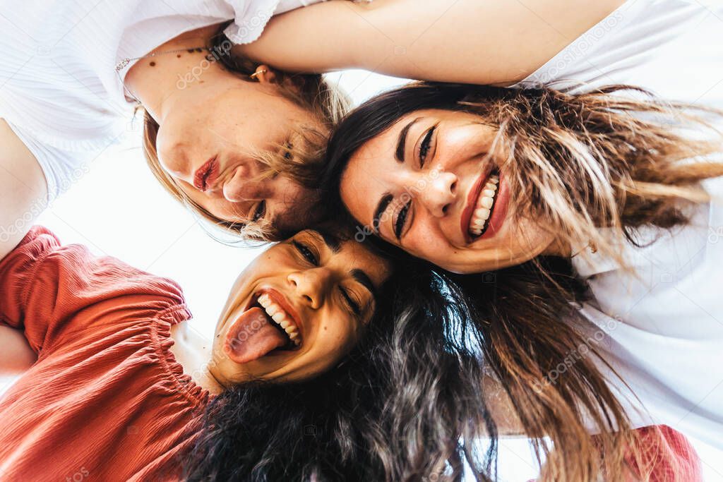 Best friends take a selfie from below with smartphone on vacation - group of happy multiracial tourists taking a funny photo - friendship and fun concept