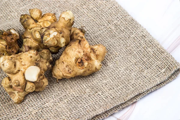 The jerusalem artichoke tuber lies on a napkin made of natural fabric on a light table. — Stock Photo, Image