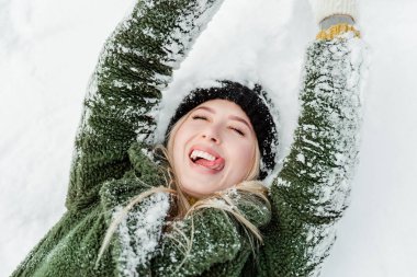 Güzel sarışın kadın, sıcacık giyinmiş, atkı ve eldivenlerle. Güzel kız karda eğleniyor.