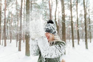 Güzel sarışın kadın, sıcacık giyinmiş, atkı ve eldivenlerle. Güzel kız karda eğleniyor.