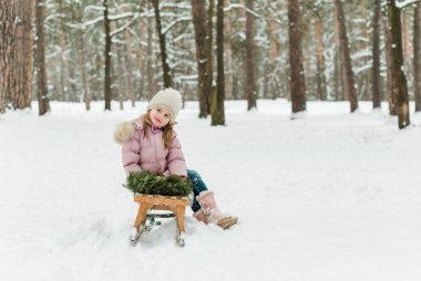 Güzel küçük kız dışarıda kışın tadını çıkarıyor. Küçük kız ormanda veya parkta kar ve kızakla eğleniyor..