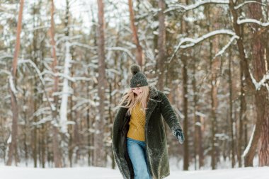Güzel sarışın kadın, sıcacık giyinmiş, atkı ve eldivenlerle. Güzel kız karda eğleniyor.