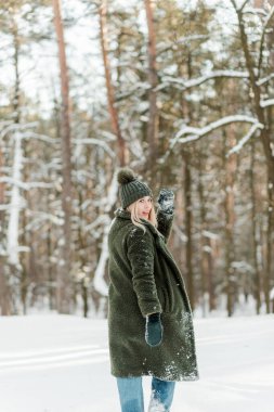 Güzel sarışın kadın, sıcacık giyinmiş, atkı ve eldivenlerle. Güzel kız karda eğleniyor.