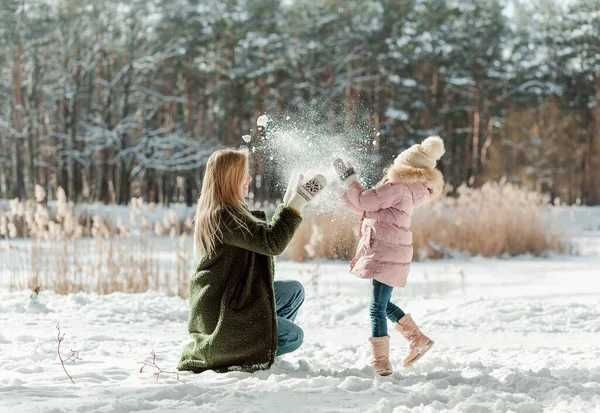 美しい母親と彼女の小さな娘は冬に雪と遊ぶ — ストック写真