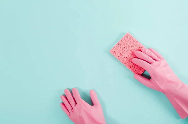 Plastik pembe eldivenli eller çamaşır süngeri tutuyor. Mavi arka plan. Oda servisi ve temizlik konsepti. Düz yatıyordu