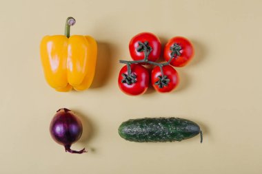 Taze sebzeler. Kiraz domatesleri, sarı dolma biber, salatalık, bej arka planda kırmızı soğan. Üst görünüm