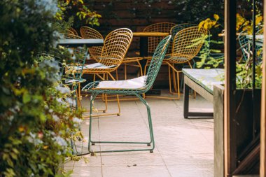 Kablodan yapılmış hasır sandalyeler fayansta bir ağacın yanında duruyor. Orada kimse yok, sıradışı sandalyeler bahçede duruyor. Metal bacaklı koltuklar. Nostaljik ve barışçıl hissediyorum. Seçici odak.
