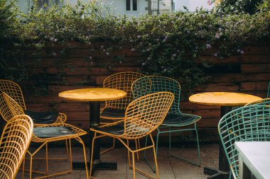 Kablodan yapılmış hasır sandalyeler fayansta bir ağacın yanında duruyor. Orada kimse yok, sıradışı sandalyeler bahçede duruyor. Metal bacaklı koltuklar. Nostaljik ve barışçıl hissediyorum. Seçici odak.