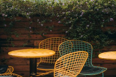 Kablodan yapılmış hasır sandalyeler fayansta bir ağacın yanında duruyor. Orada kimse yok, sıradışı sandalyeler bahçede duruyor. Metal bacaklı koltuklar. Nostaljik ve barışçıl hissediyorum. Seçici odak.