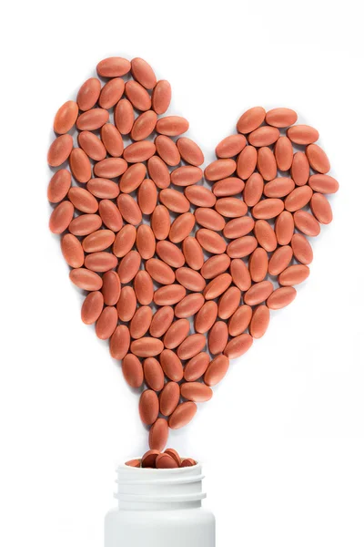 A forma di cuore di pillole rosse che fuoriescono da una bottiglia di medicinale — Foto Stock