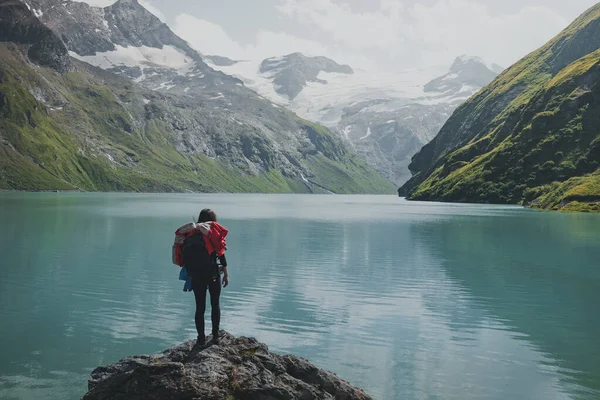 一个年轻的女徒步旅行者背着背包看风景的场景 在后视镜中 女性可以看到湖水和高山 奥地利卡普龙Stausee Mooserboden美丽的绿松石水 — 图库照片