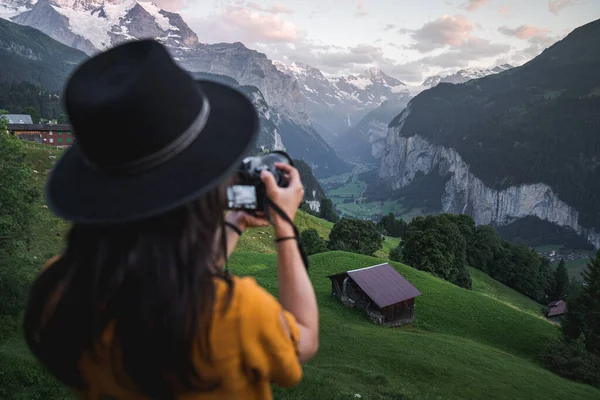 Günbatımında Wengen 'deki ünlü turistik mekanda dijital kamerayla fotoğraf çeken genç bir kadın turist. Lauterbrunnen Vadisi üzerinde yeşil tarlaları ve karlı dağları olan ünlü Instagram yürüyüş yeri