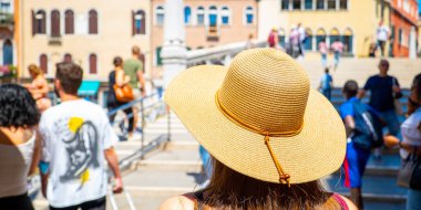 A woman with a hat walking in Venice on a sunny summer and holiday day.