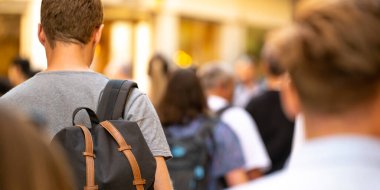 Genç bir öğrenci kalabalığın arasında sırt çantasıyla yürüyor.