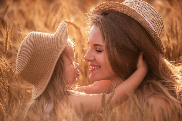麦畑のスライスでわら帽子の母親と娘のクローズアップ肖像画 小さな女の子がキスをし ライ麦の小穂に若い女性を抱きます 自然の農業のテクスチャ 女の子は楽しい 笑いを持っている — ストック写真