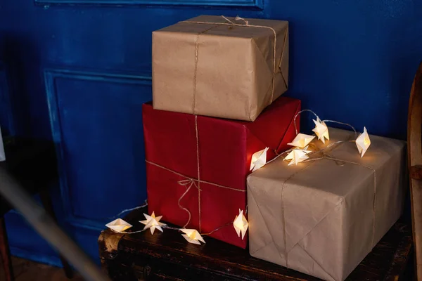 在木制圣诞桌上 礼物包在牛皮纸上 用绳子绑在一面深蓝色的墙的后面 盒子上躺着一个星形的明亮的花环 节日包装设计 — 图库照片