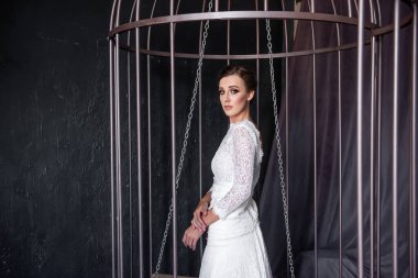 Demir bir kafeste moda gelini, mutsuz bir şekilde parmaklıkların arkasından dışarı bakıyor. İradesiz bir hayat. Uydurma bir mantık evliliği. Rahat bölgenden çık. Ataerkil evlilik kavramı. Boşluğu kopyala