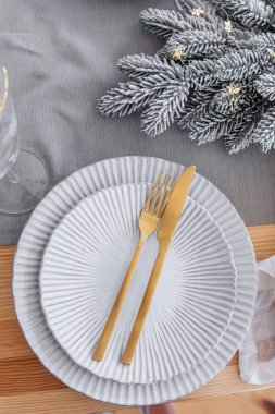 Yeni yıl kutlaması masası üst görünümü ayarlıyor. Ahşap bir masanın üzerinde gri bir masa örtüsü, beyaz dalgalı tabaklar, altın çatal, bıçak bulunur. Karlı Noel şubesi. Uzayı kopyala Modaya uygun iç mekan.